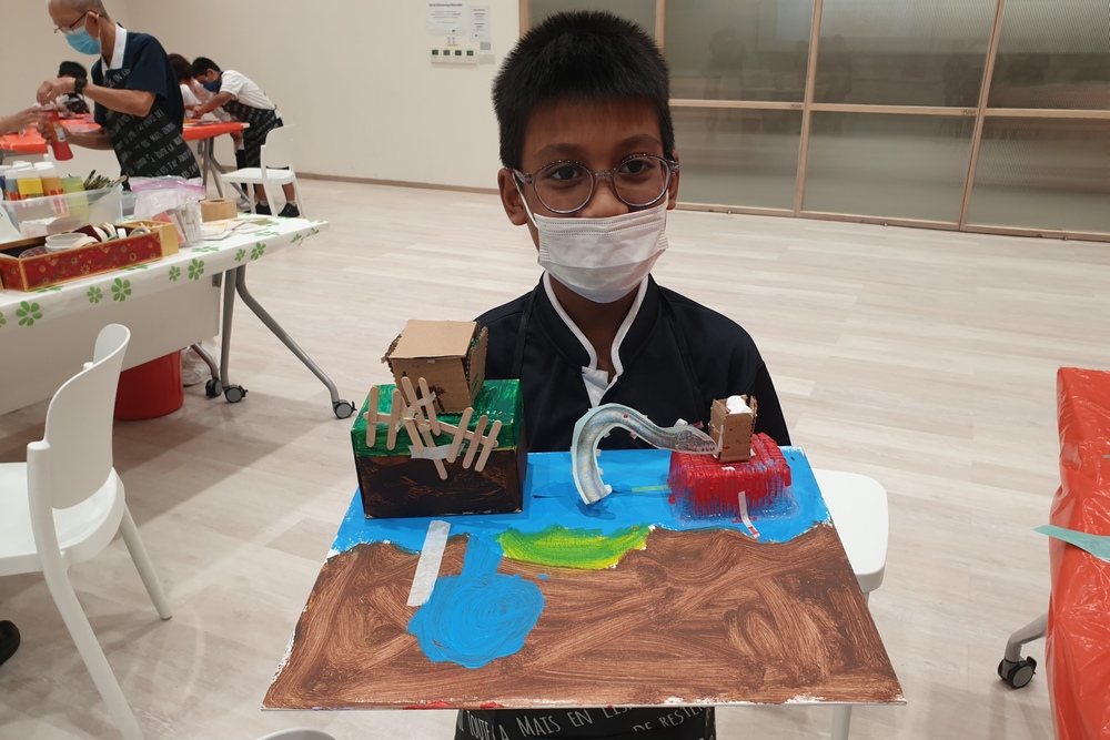 Kidz Hideout participant Qaiser Haiziq Hasrizan proudly showing his artwork which he was working on before the exhibition. (Photo by Sharifah Faizah)